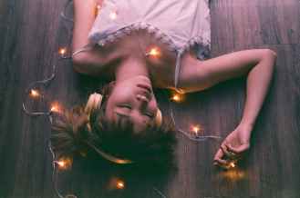 woman in white sleeveless shirt lying on wooden surface with fairy lights